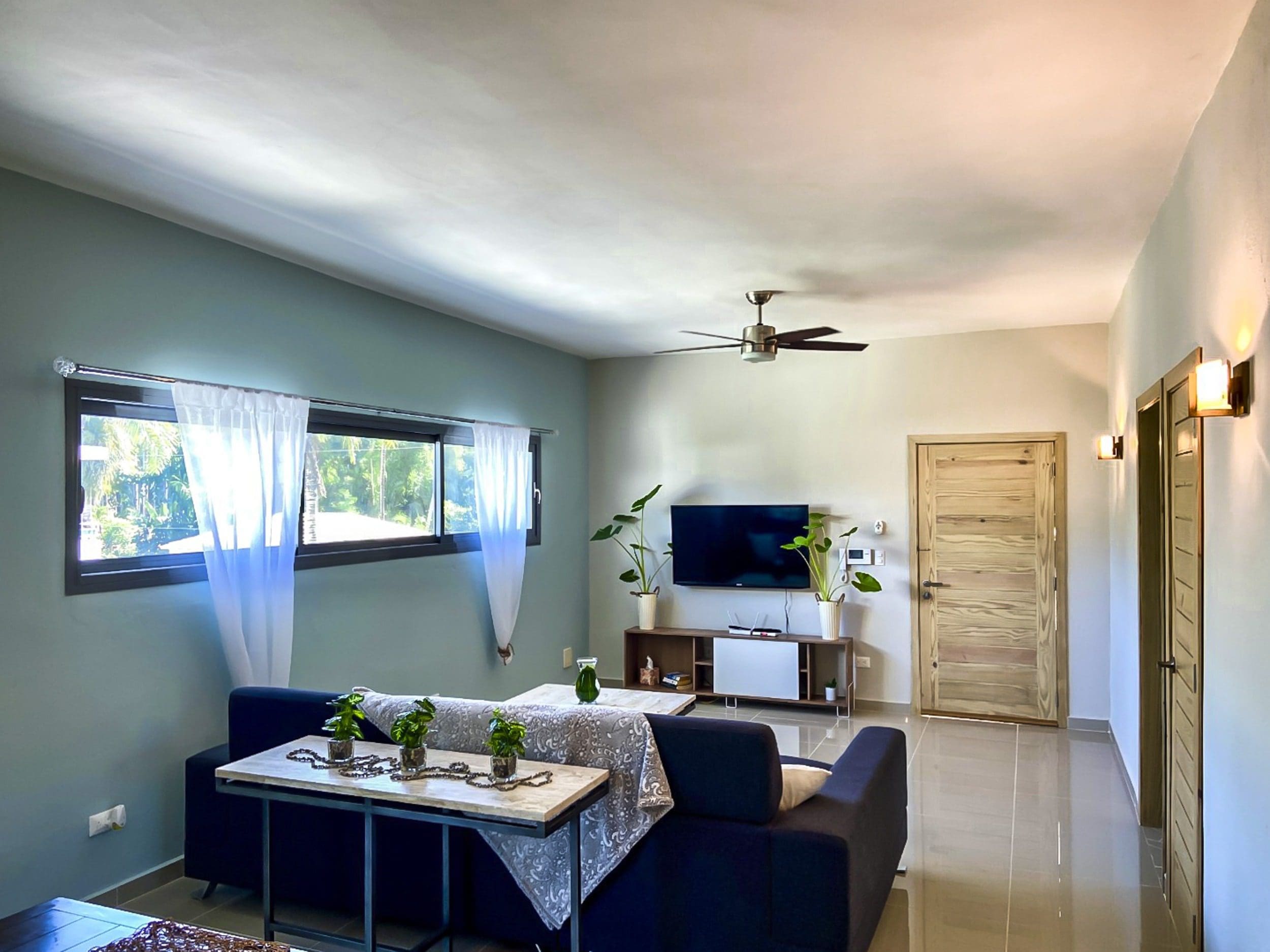 buyDRproperty Modern living room with blue sofa, TV, and windows. For sale! 2 Bedroom Penthouse in ProCab Sosua Real Estate