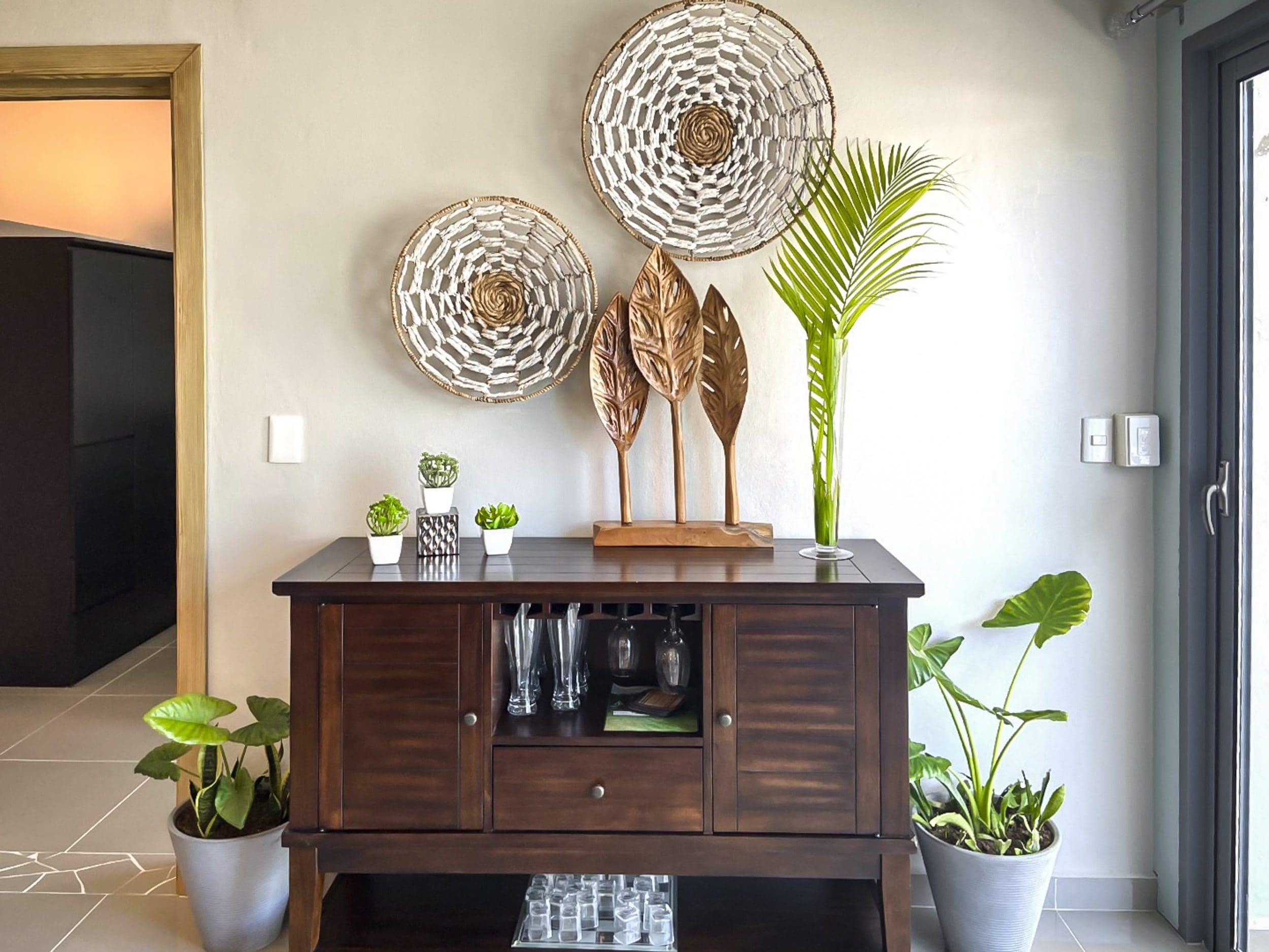 buyDRproperty Stylish dark wood cabinet with decorative wall hangings. Plants add a touch of greenery. Sosua Real Estate