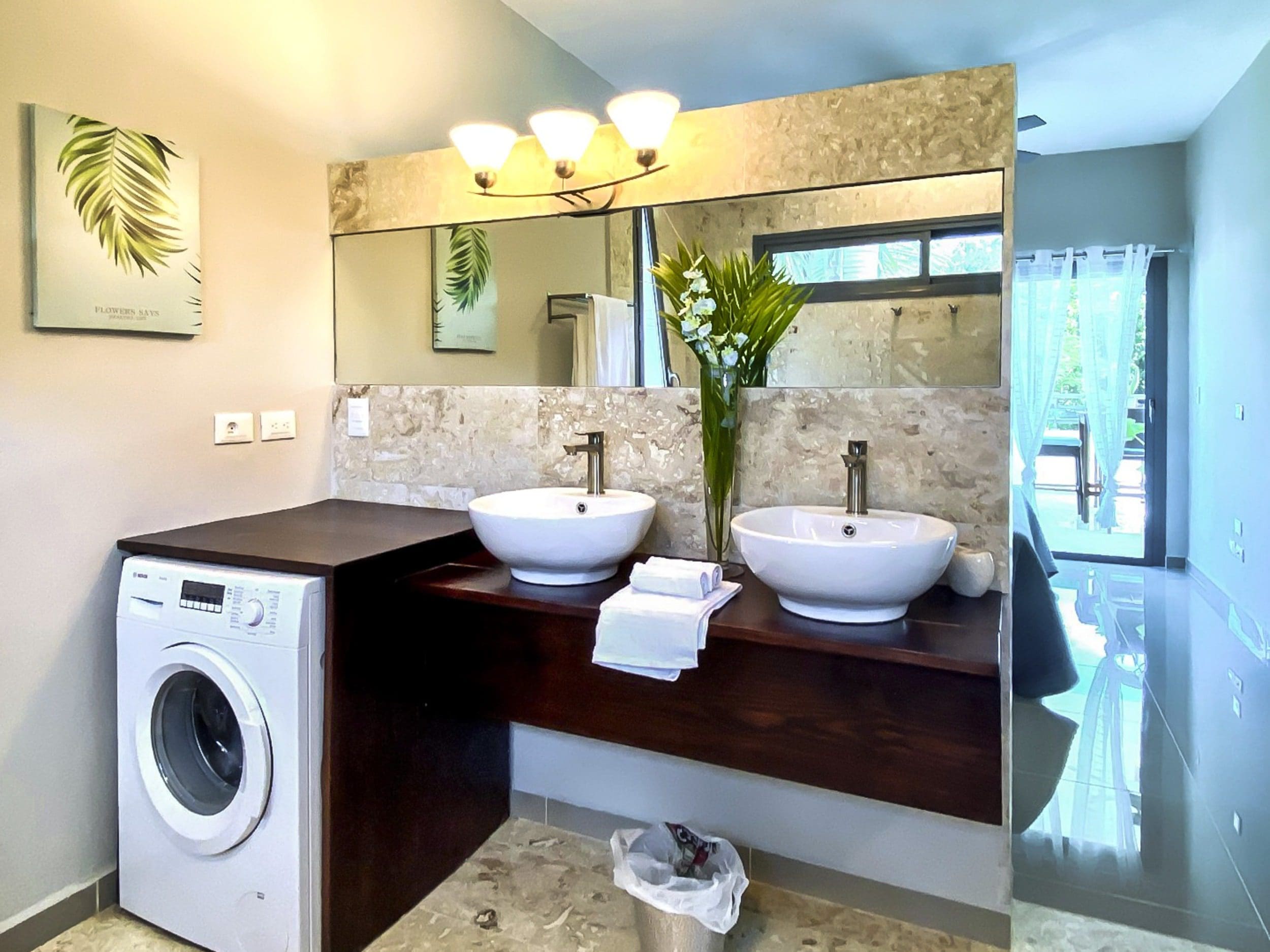 buyDRproperty Modern bathroom with double sinks, washing machine, and balcony access. Sosua Real Estate
