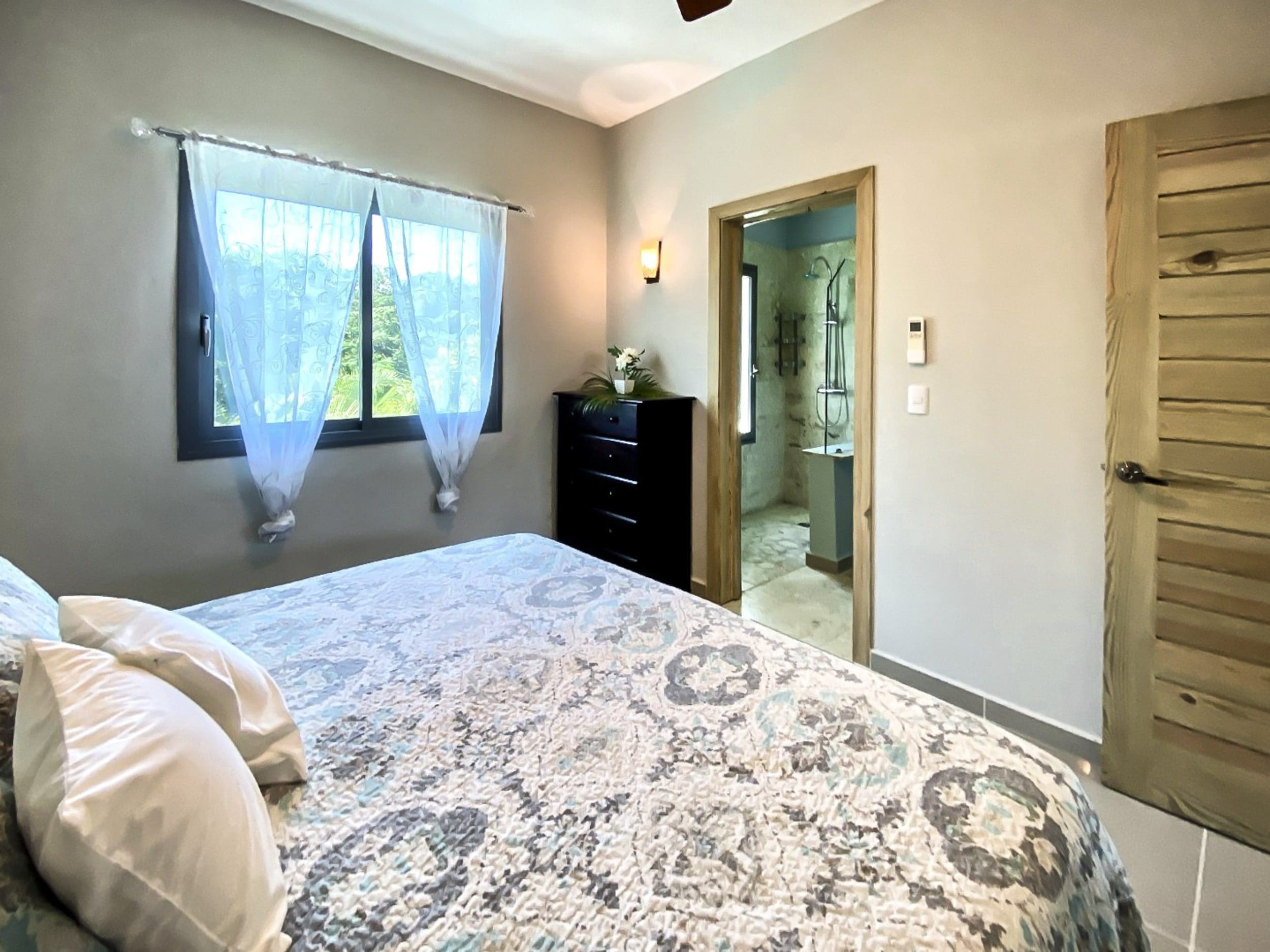 buyDRproperty Bedroom with bed, window, and doorway to bathroom. Modern design. Sosua Real Estate