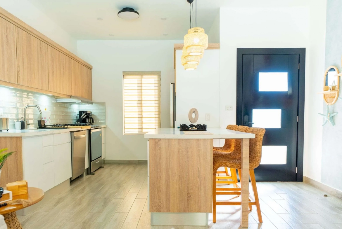 buyDRproperty Modern kitchen with light wood cabinets, white countertops, and a breakfast bar with rattan stools. Sosua Real Estate