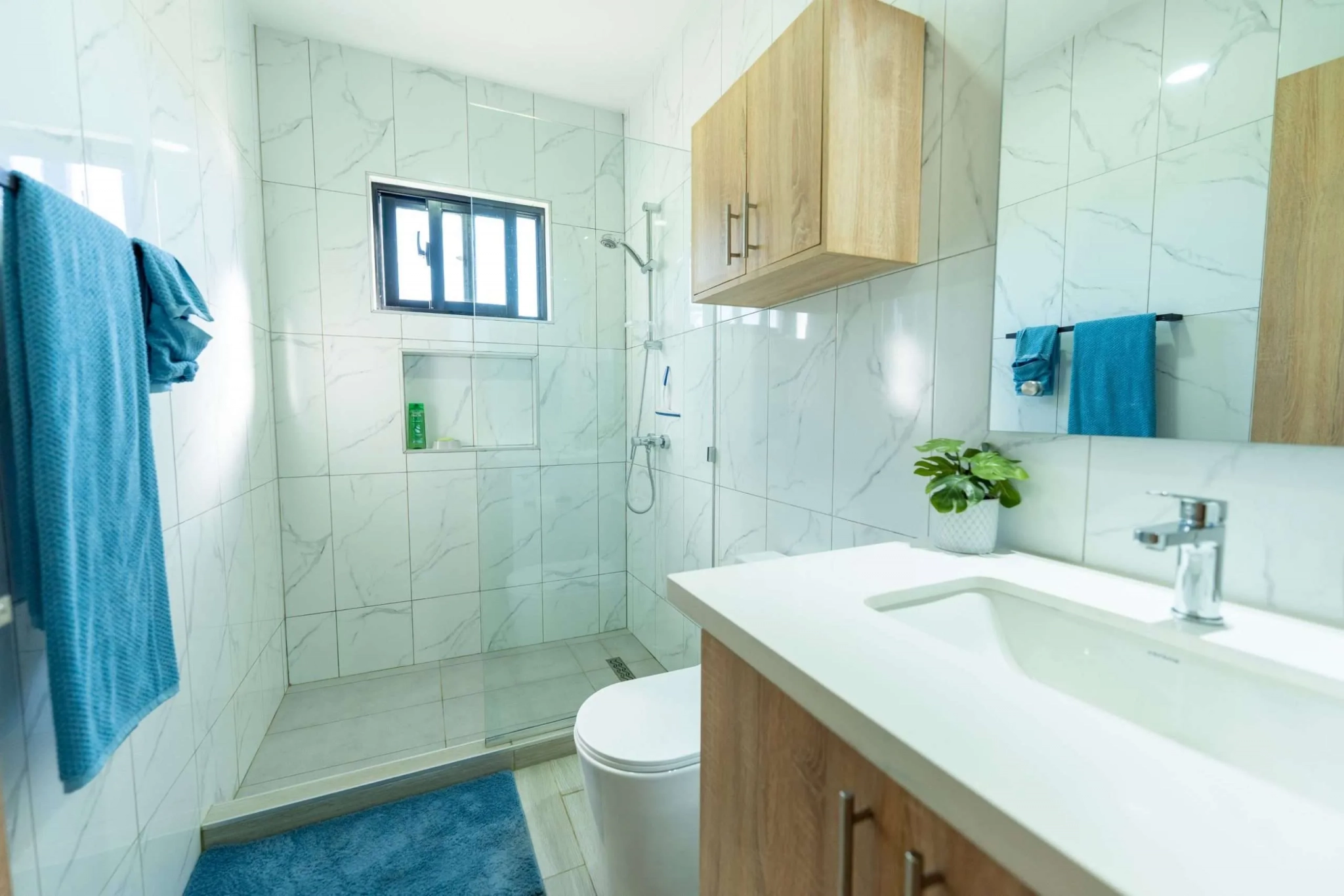 buyDRproperty Modern bathroom with white marble tiles, walk-in shower, and wooden vanity. Sosua Real Estate
