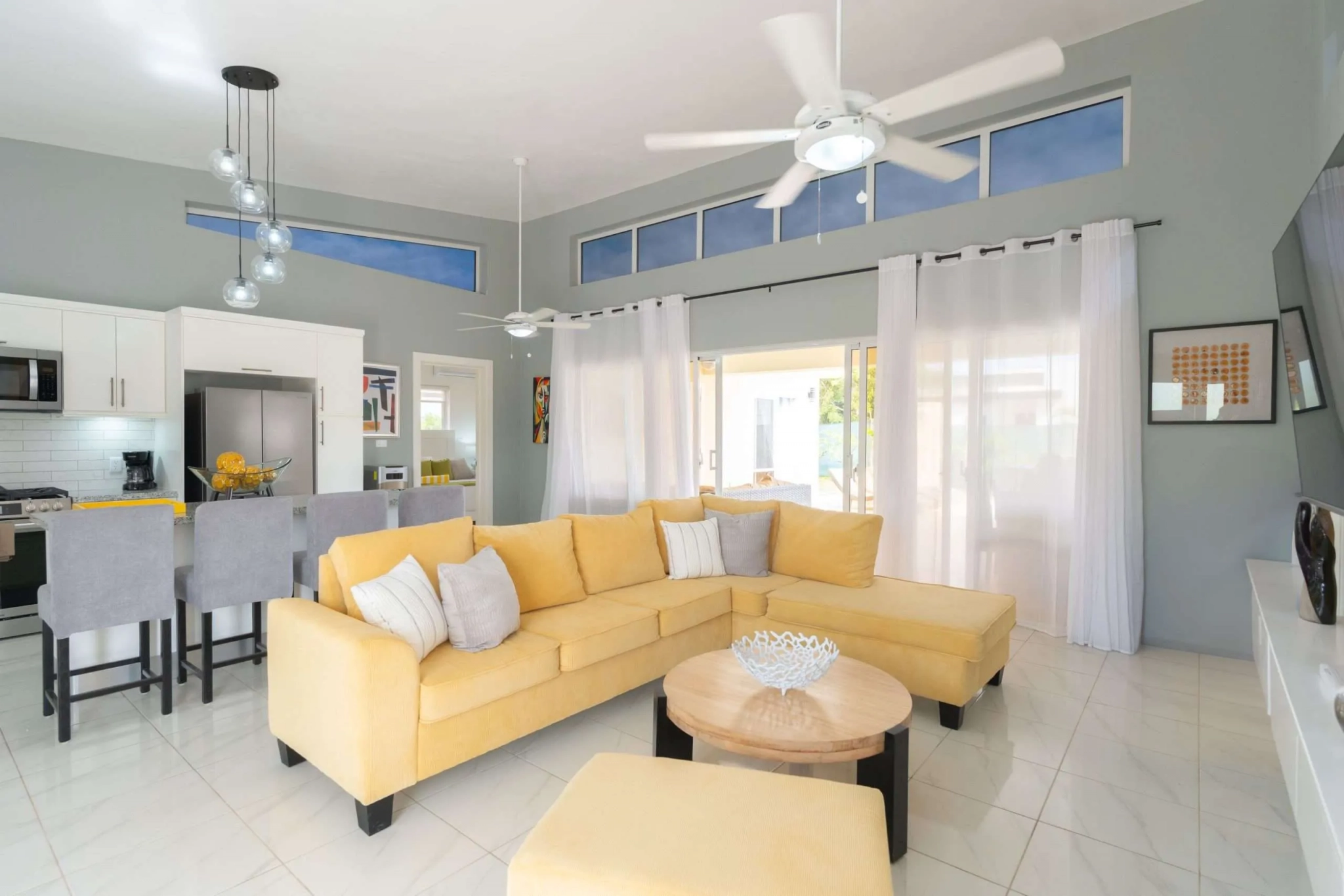 buyDRproperty Bright, modern living room with a yellow sectional sofa, ceiling fans, and kitchen island Sosua Real Estate