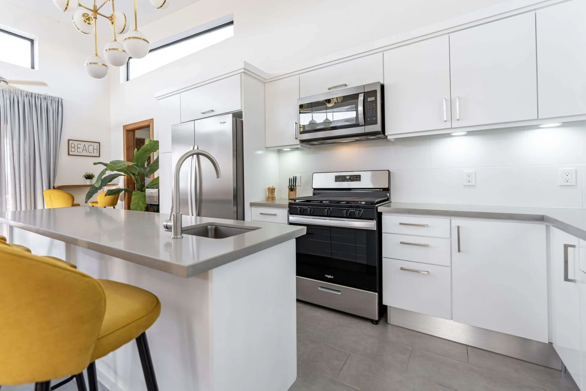 buyDRproperty Modern white kitchen with stainless steel appliances, island, and yellow stools. Sosua Real Estate