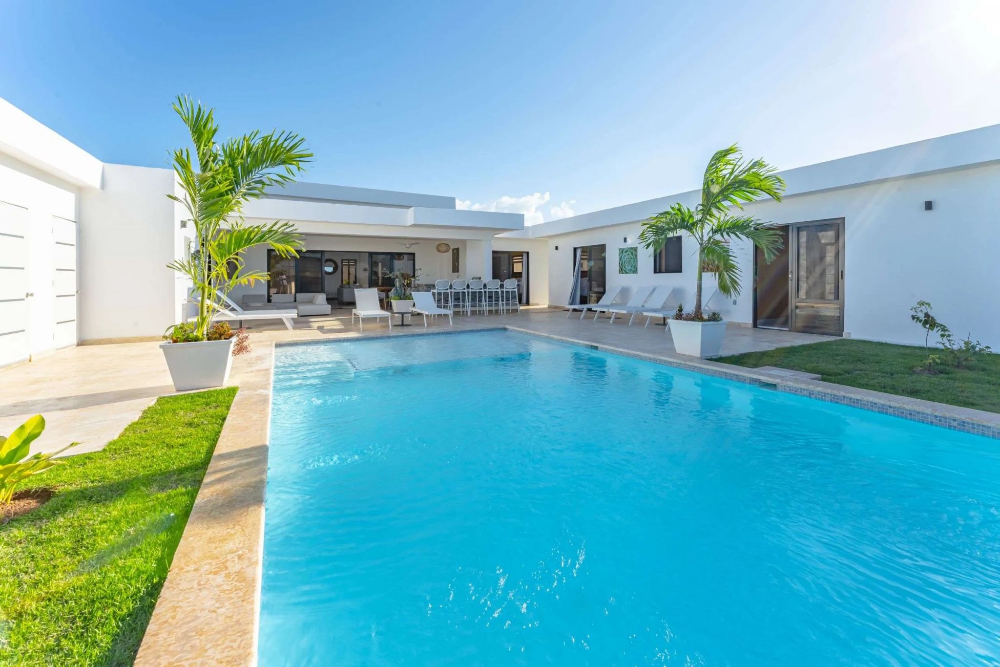 buyDRproperty Modern villa courtyard with a bright blue swimming pool and palm trees. Sosua Real Estate