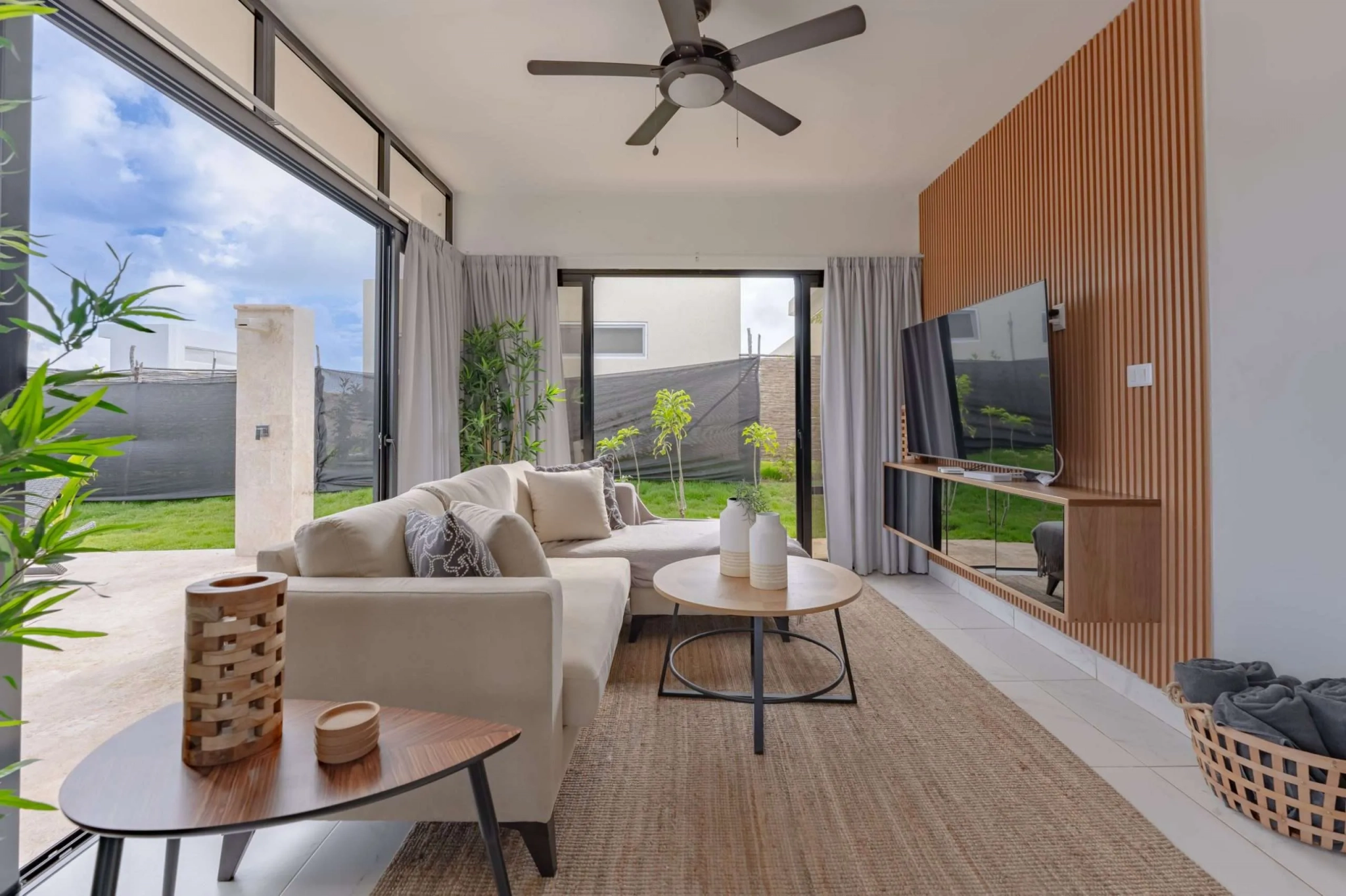 buyDRproperty Modern living room with sectional sofa, TV, and large sliding glass doors opening to a backyard. Sosua Real Estate