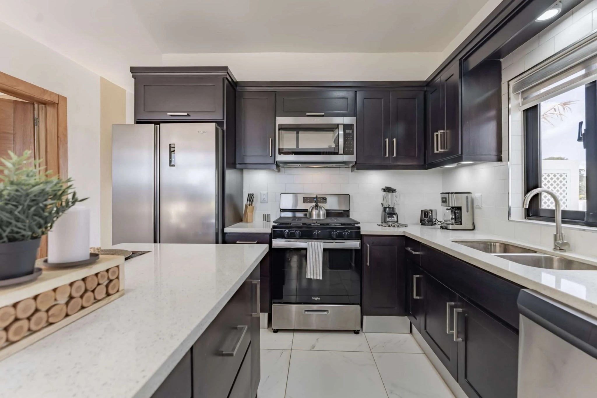 buyDRproperty Modern dark wood kitchen with stainless steel appliances and white quartz countertops. Sosua Real Estate
