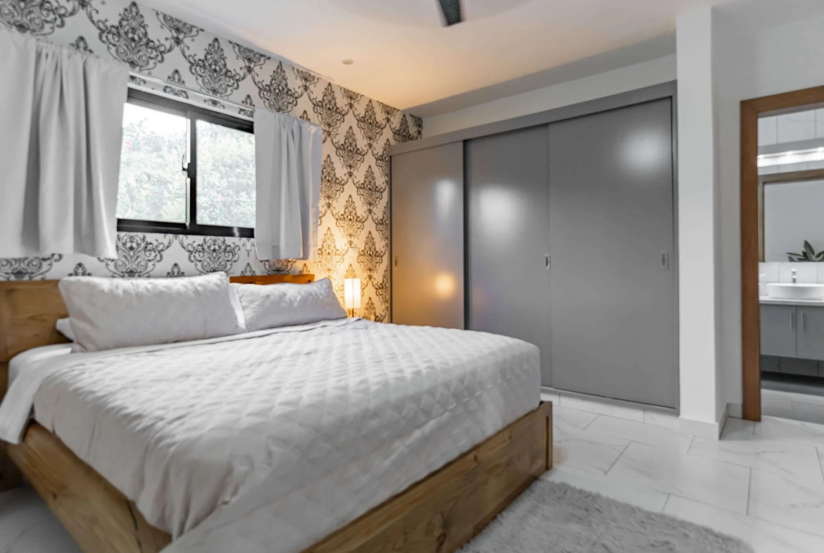 buyDRproperty Modern bedroom with a king-size bed, patterned wallpaper, and sliding closet doors. Sosua Real Estate
