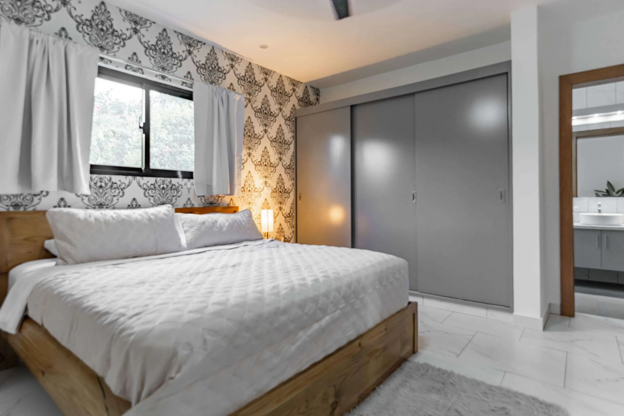 buyDRproperty Modern bedroom with a king-size bed, patterned wallpaper, and sliding closet doors. Sosua Real Estate