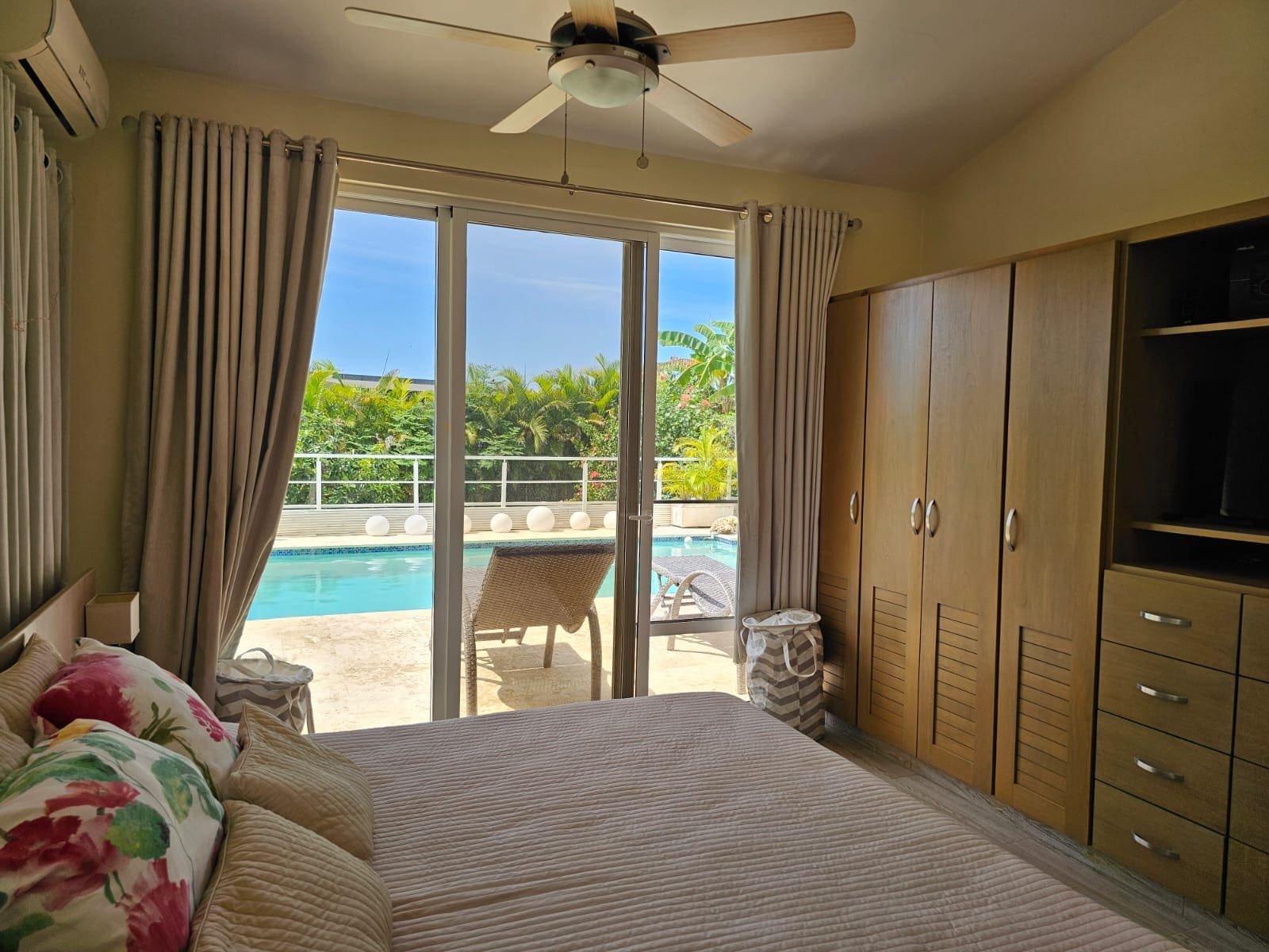 buyDRproperty Bedroom with king-size bed and pool view, tropical foliage, and ceiling fan. Sosua Real Estate