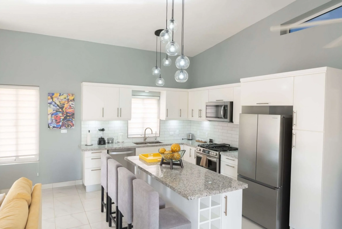 buyDRproperty Modern white kitchen with granite island, stainless steel appliances, and pendant lights. Sosua Real Estate
