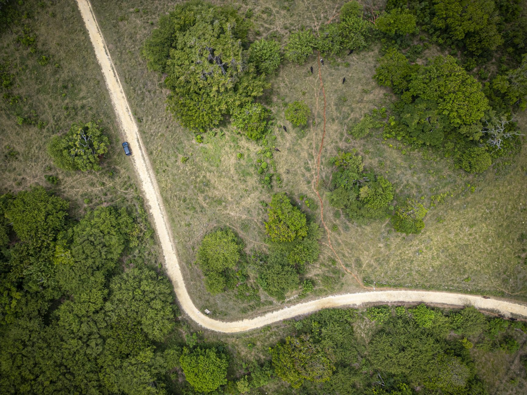 buyDRproperty Aerial view of a winding dirt road through a rural landscape, with a vehicle parked on the side. Sosua Real Estate