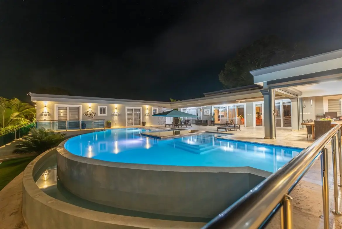 buyDRproperty Luxury villa with illuminated pool at night, featuring modern architecture and outdoor seating. Sosua Real Estate