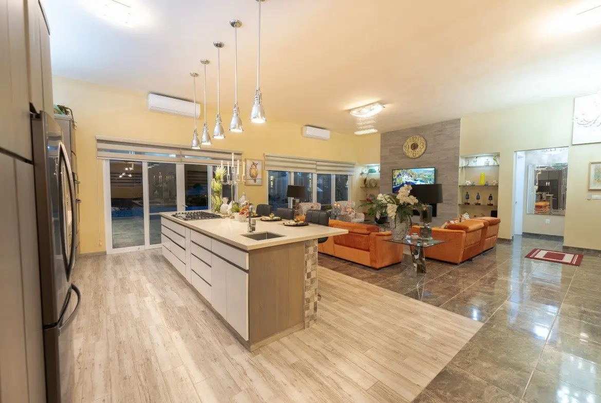 buyDRproperty Modern open-plan kitchen and living room with island, orange sofas, and pool view. Sosua Real Estate