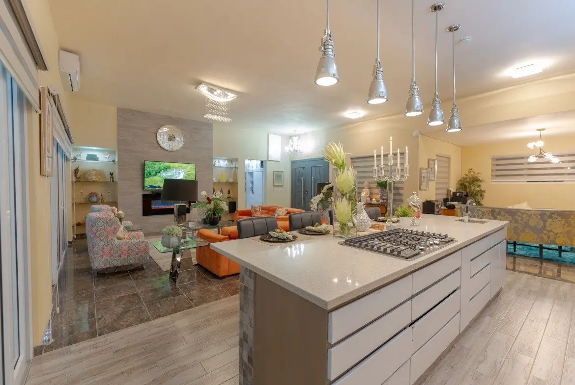 Open-concept kitchen and living area with a large white island, pendant lights, and a long dining counter in a bright, modern home.