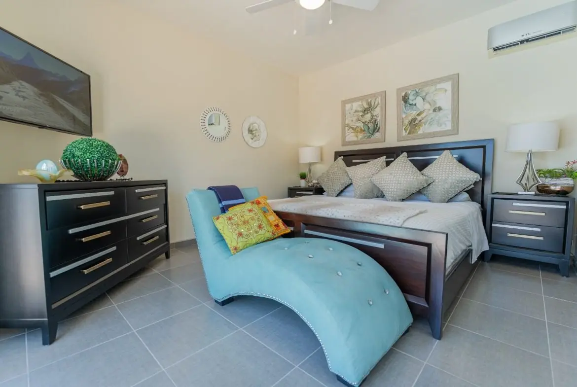 Modern bedroom with dark wood bed, two dressers, and a turquoise chaise at the foot of the bed.