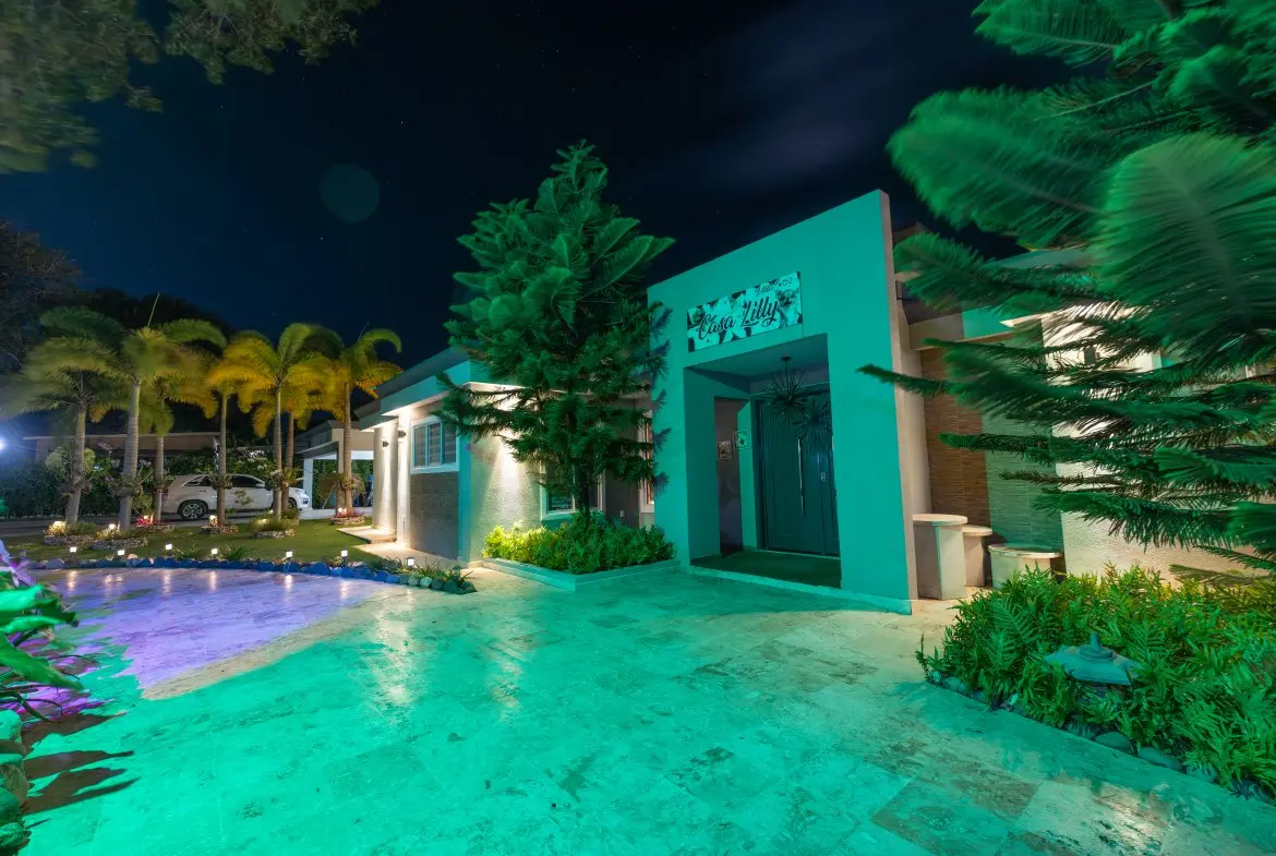 buyDRproperty Eagle Hills mansion at night, illuminated with colorful lights and palm trees Sosua Real Estate